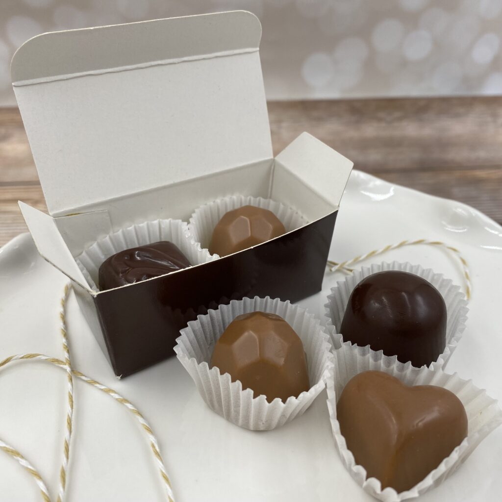 A box of chocolate bonbons next to individual bonbons of various shapes and colors